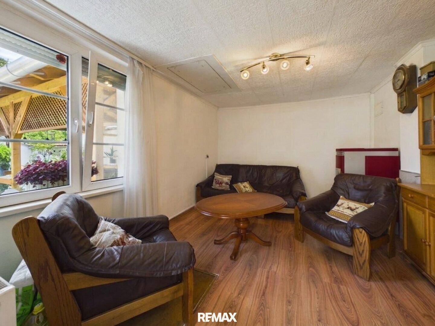 Gemütlicher Wohnraum mit Ledersesseln, Sofa und Holzboden, mit Blick auf den überdachten Außenbereich.