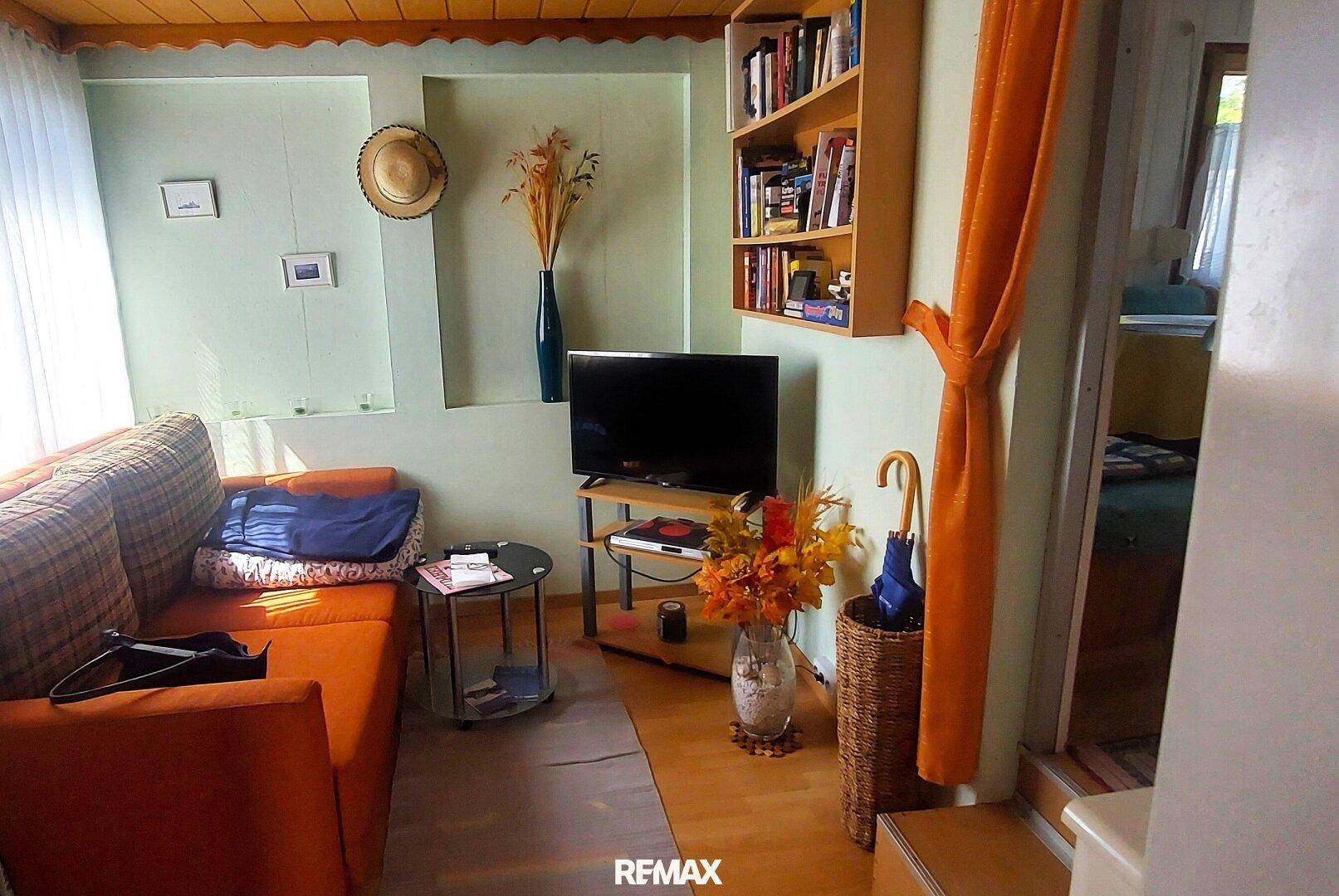 Gemütliches Wohnzimmer mit Sofa, Fernseher, Bücherregal und Holzdecke, ausgestattet mit Parkettboden.