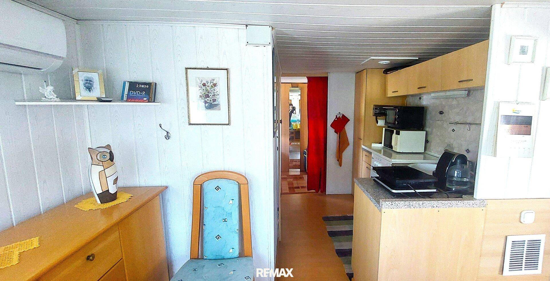 Übergangsbereich mit Klimaanlage, Regal und Blick in die angrenzende Küche, mit Holzdecke.