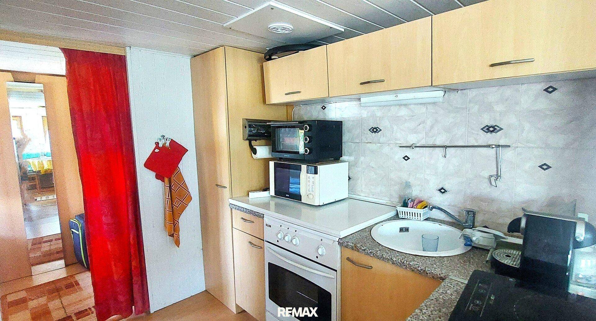 Kleine Küche mit Einbauschränken, Backofen, Mikrowelle und Spülbecken, mit Fliesenboden.