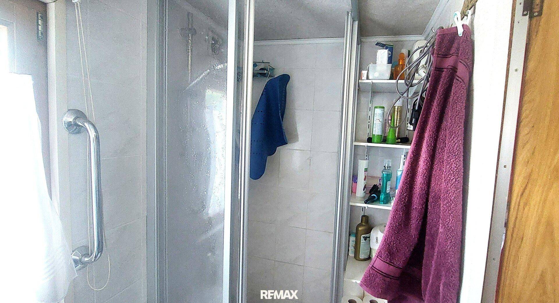 Badezimmer mit Duschkabine, Haltegriffen und Ablagemöglichkeiten für Pflegeprodukte, mit hellen Fliesen.