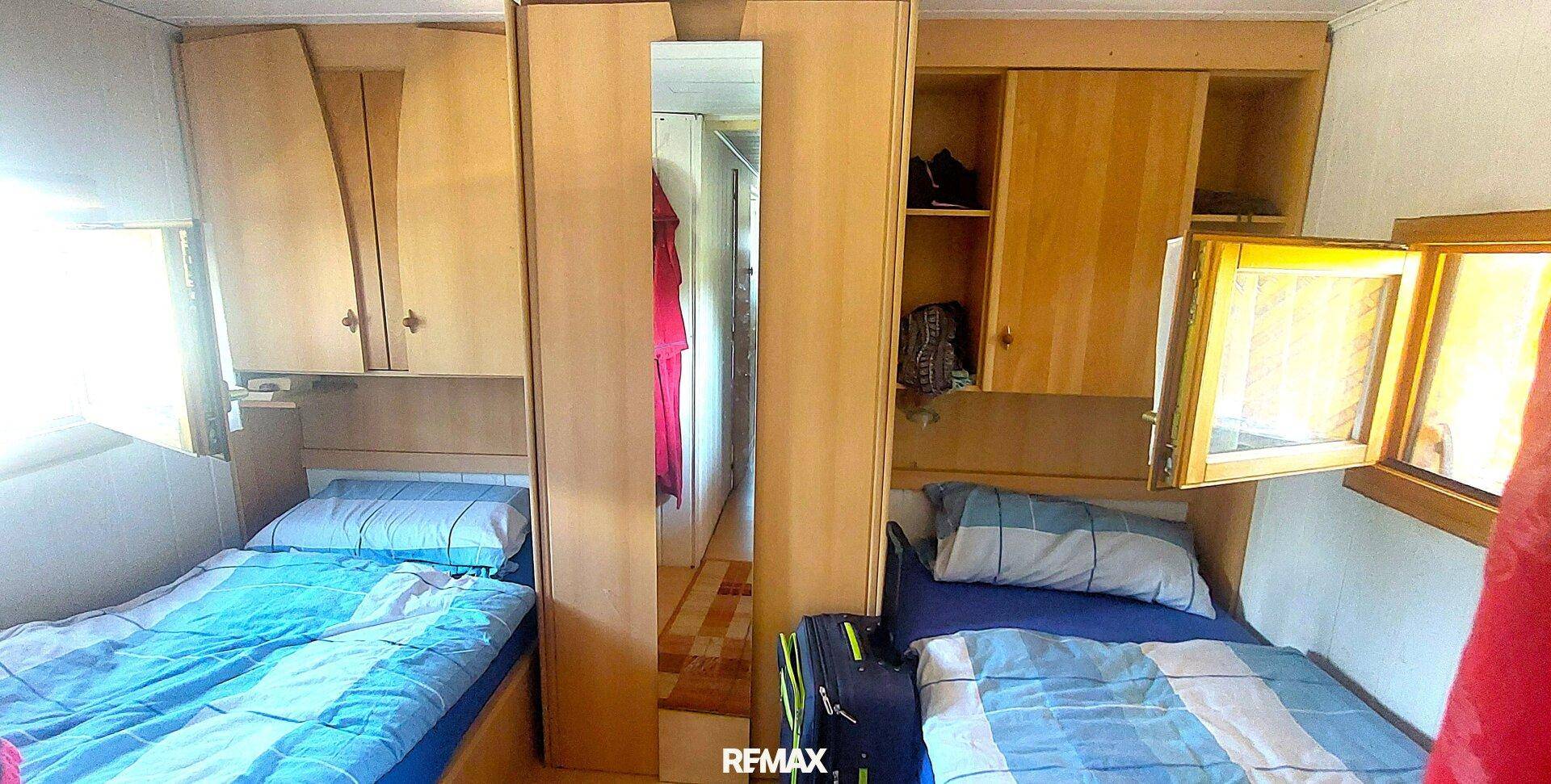 Schlafzimmer mit zwei Einzelbetten, Einbauschränken und einem Spiegel, mit Parkettboden und Fenster.