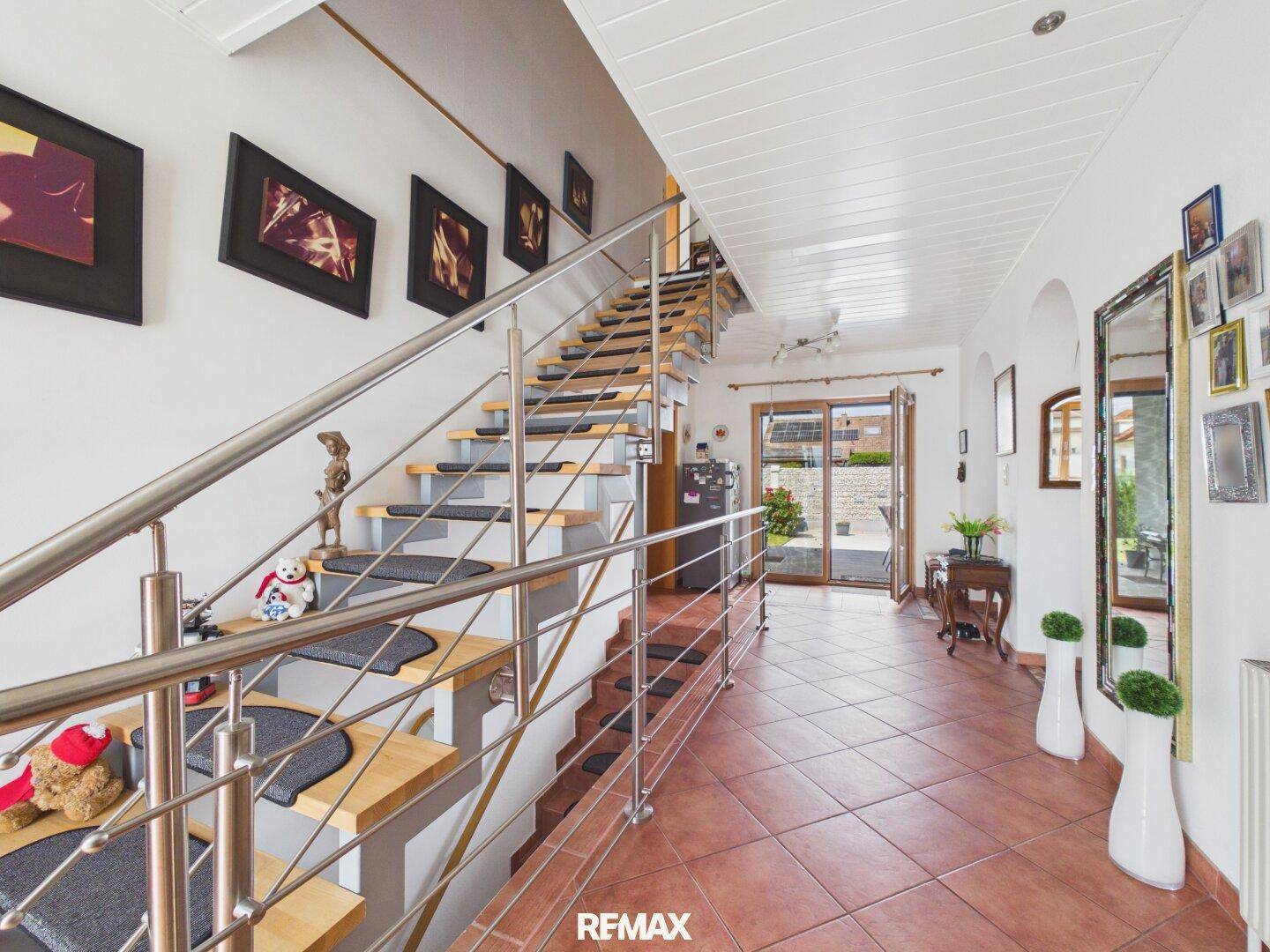 Heller Eingangsbereich mit moderner Treppe aus Holz und Edelstahl sowie Terrakotta-Fliesenboden.