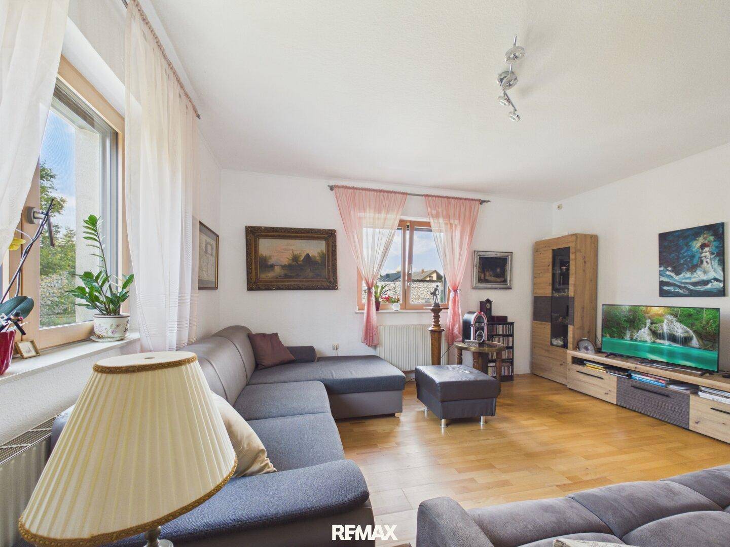 Gemütliches Wohnzimmer mit großem Ecksofa, Holzboden und Fenstern mit Vorhängen.