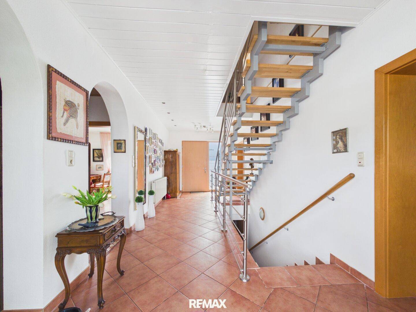 Geräumiger Flur mit offener Treppe, Terrakotta-Fliesen und dekorativen Elementen.