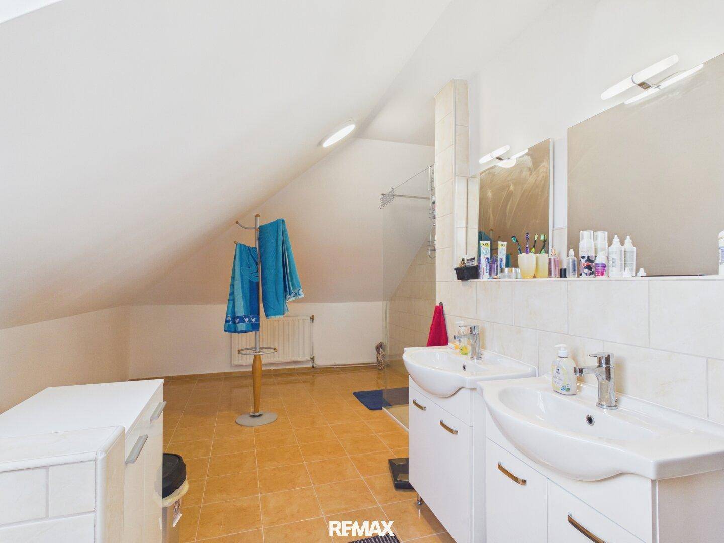 Modernes Badezimmer im Dachgeschoss mit Doppelwaschbecken, Fliesenboden und Dachschräge.