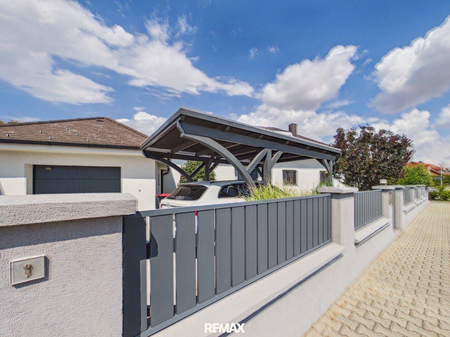 Seitenansicht des Hauses mit Carport, modernem Zaun und Einfahrt.