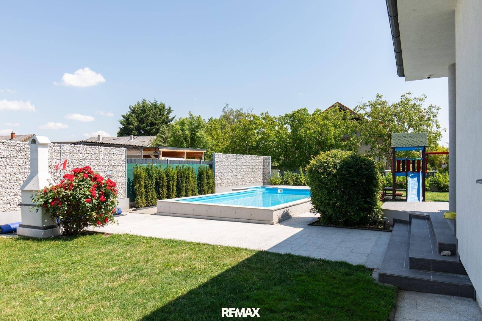 Großer Gartenbereich mit Pool, Rasenfläche, Grillplatz und Kinderspielplatz.