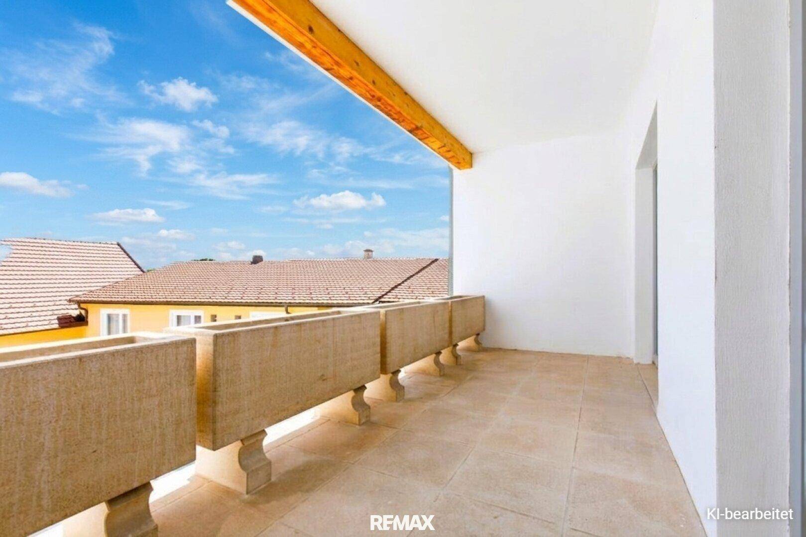 Großer Balkon mit Fliesenboden und Blick auf die umliegenden Dächer unter blauem Himmel.