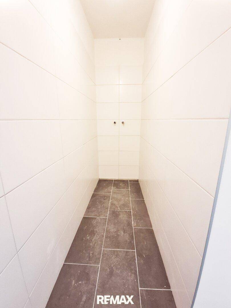 Schmaler Raum mit dunklen Bodenfliesen und weißen Wandfliesen, vorbereitet für eine Dusche.