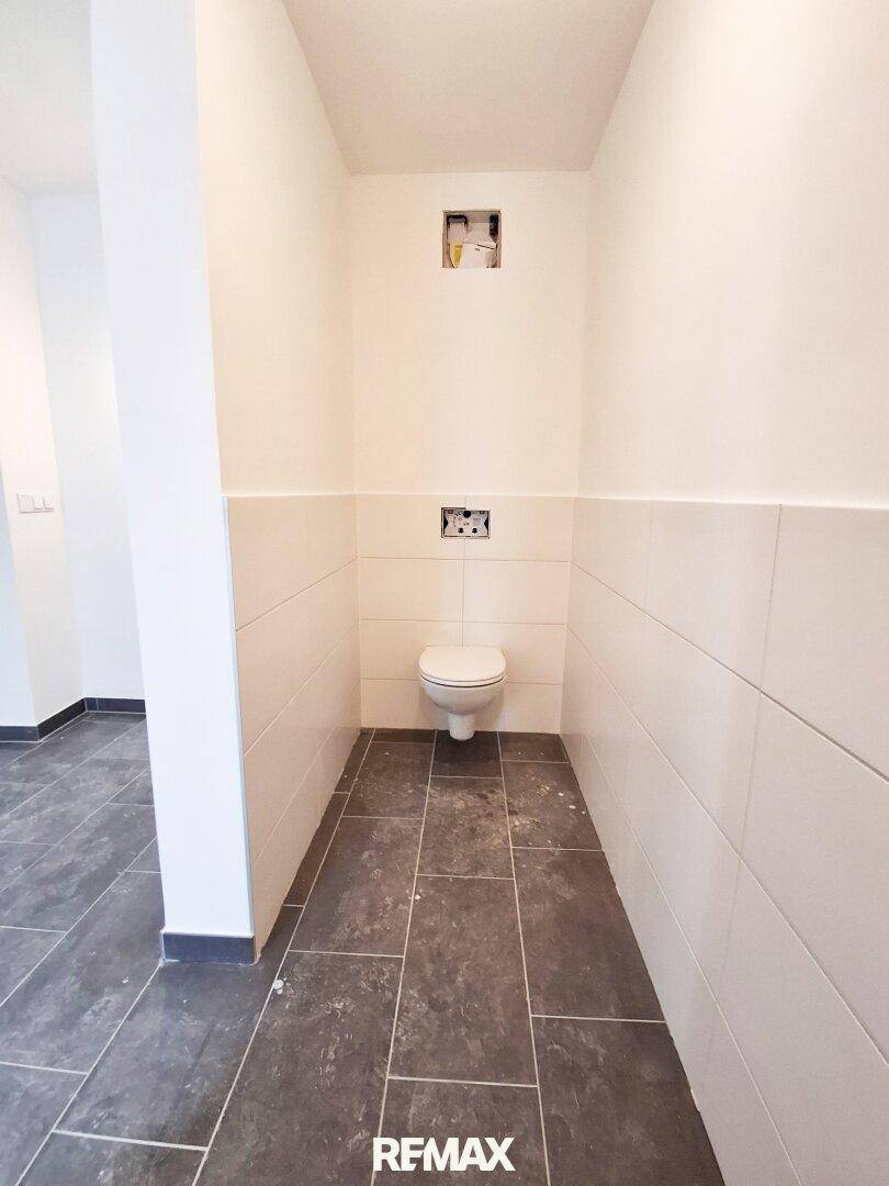Modernes WC mit wandhängender Toilette, dunklen Bodenfliesen und weißen Wandfliesen.