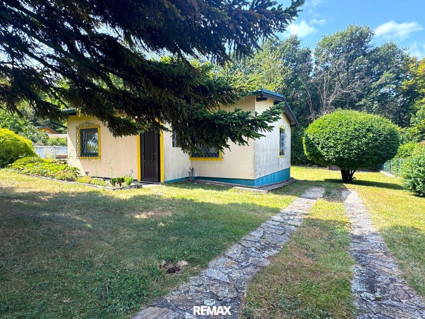 Ansicht des Hauses von der Seite mit Rasenfläche und Bäumen im Hintergrund.