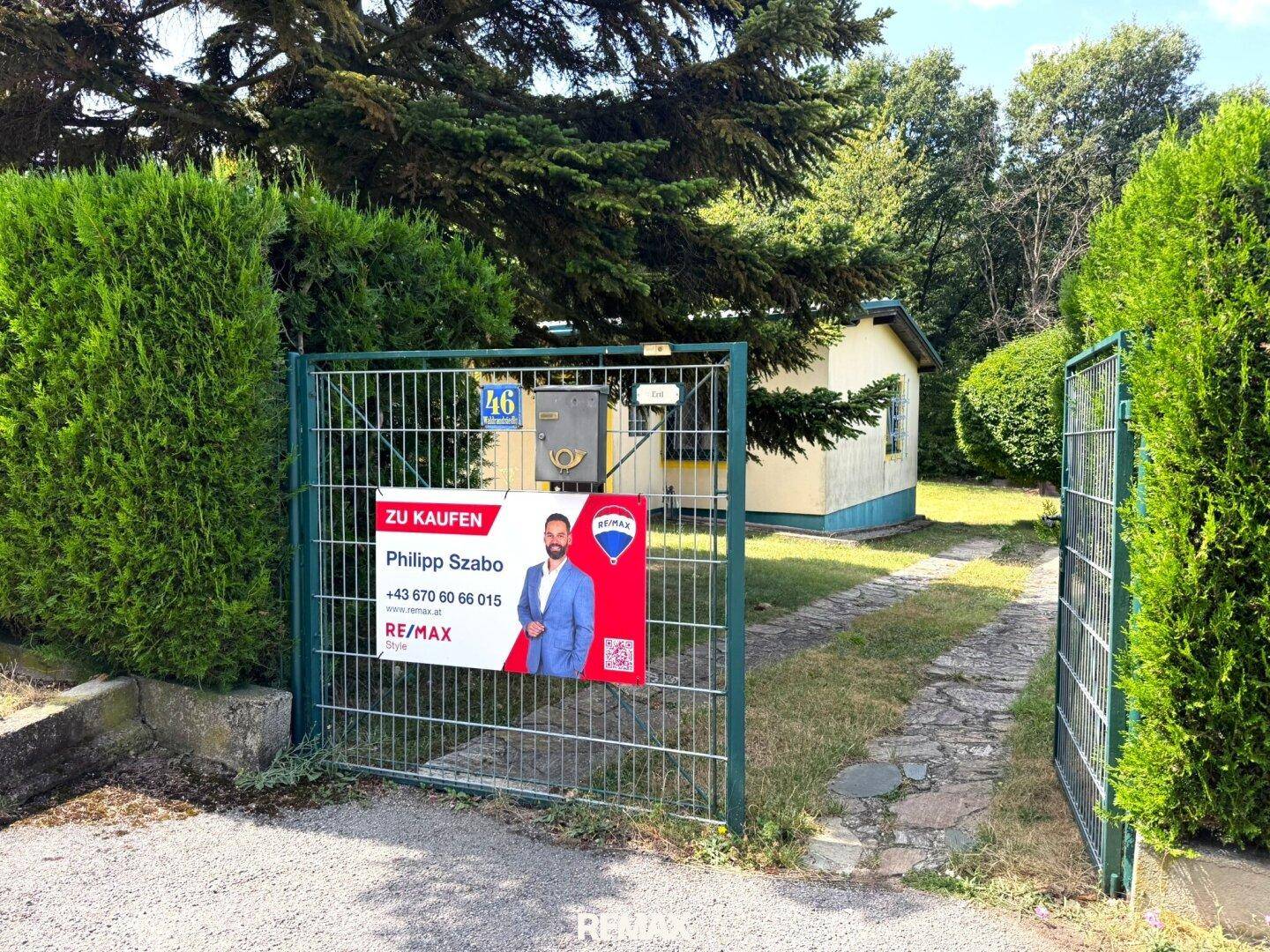 Eingangstor zum Grundstück mit "Zu Kaufen" Schild und Blick auf das Haus.