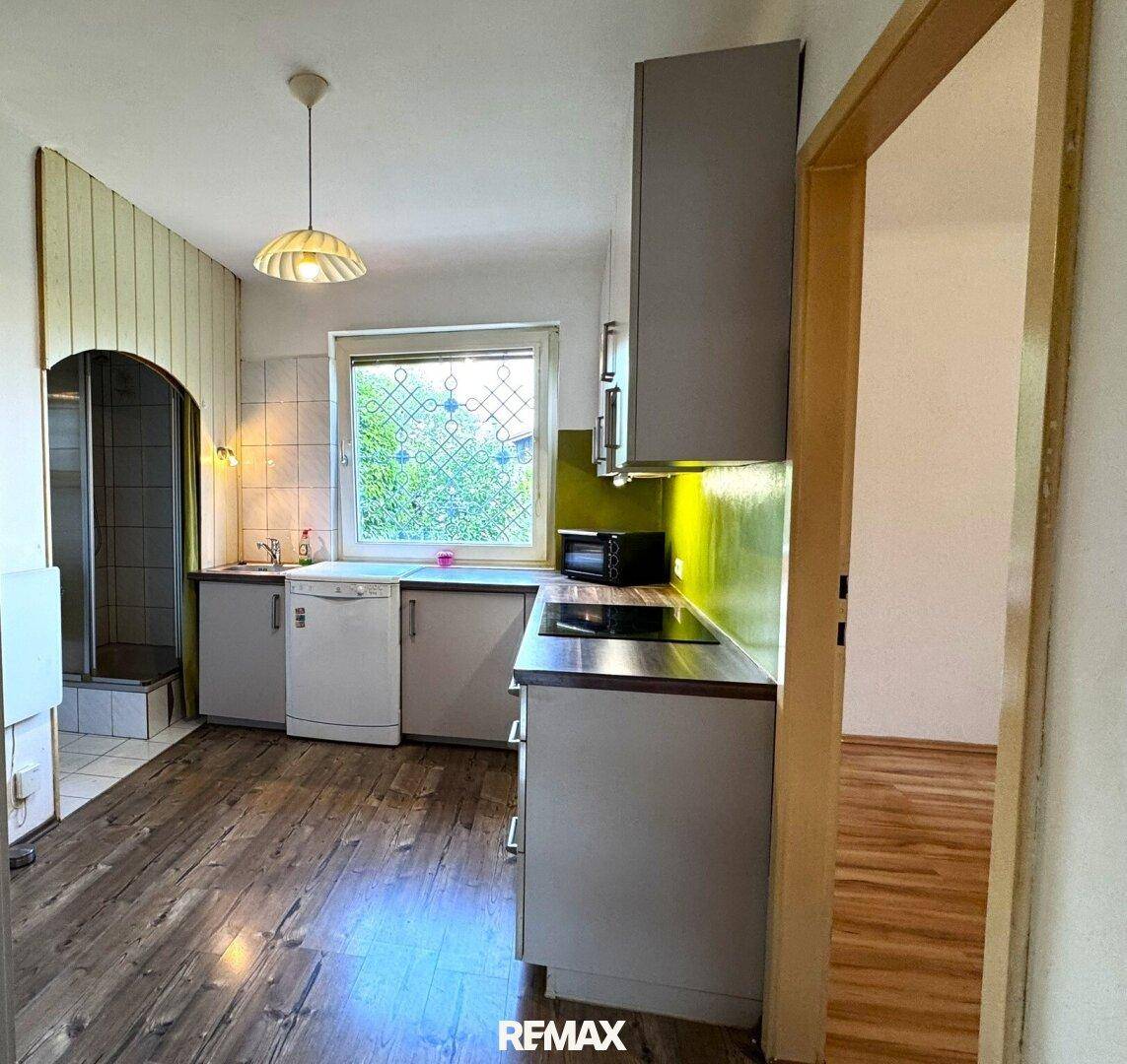 Funktionale Küche mit Holzoptikboden, grüner Rückwand und Einbaugeräten.