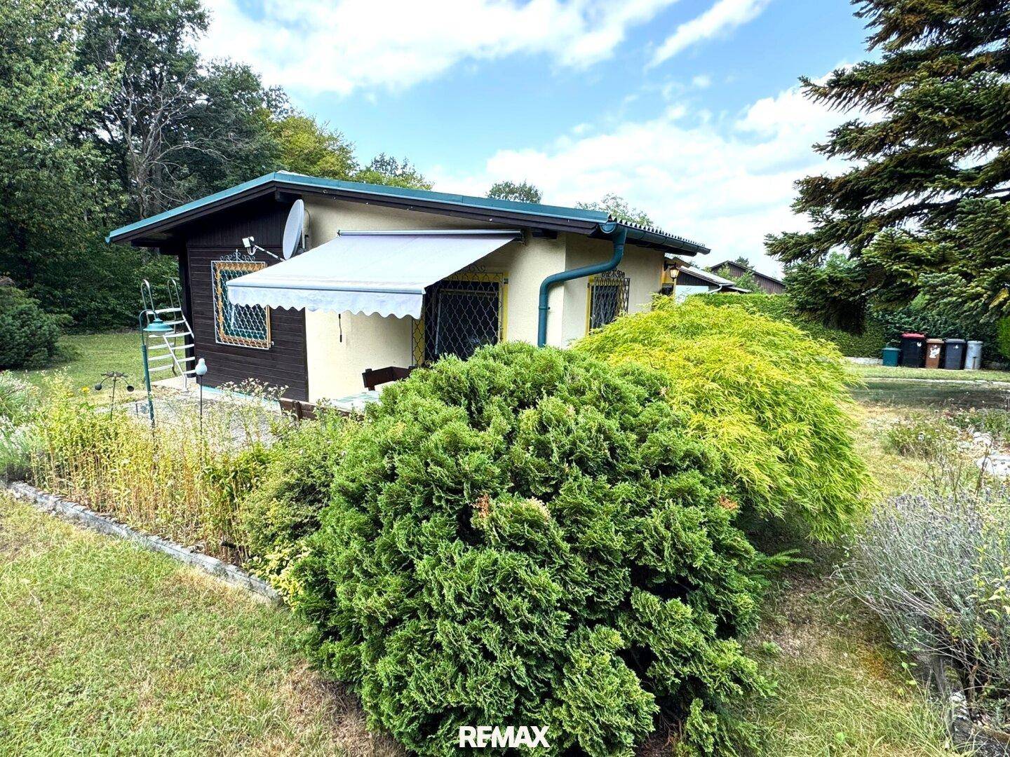 Seitenansicht des Hauses mit Markise über einem Fenster und umgebender Vegetation.