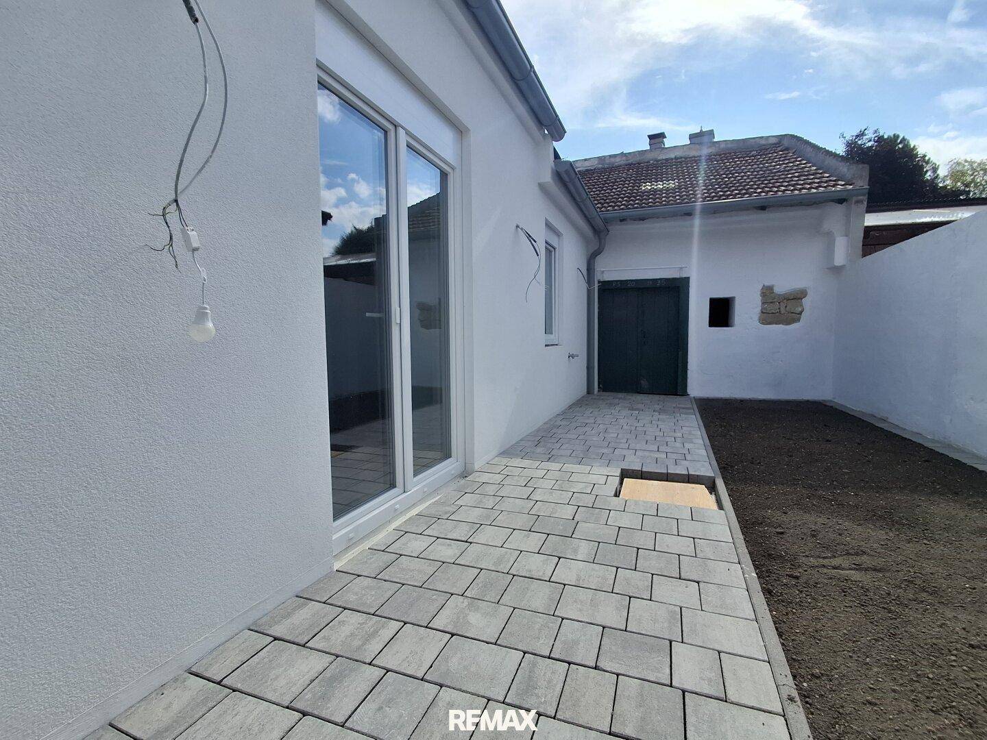 Frisch gepflasterter Terrassenbereich mit großzügiger Glastür zum Innenraum und vorbereitetem Gartenland.