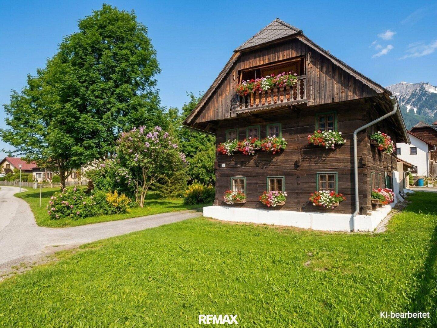 Charmantes Holzhaus mit blühenden Blumenkästen und Bergblick in sonniger Landschaft.