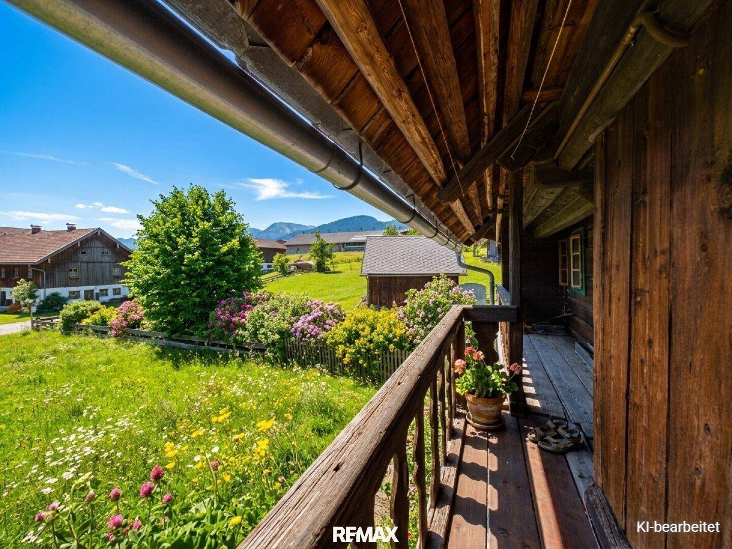 Sonniger Holzbalkon mit Blumen und weitem Blick auf die grüne Landschaft.