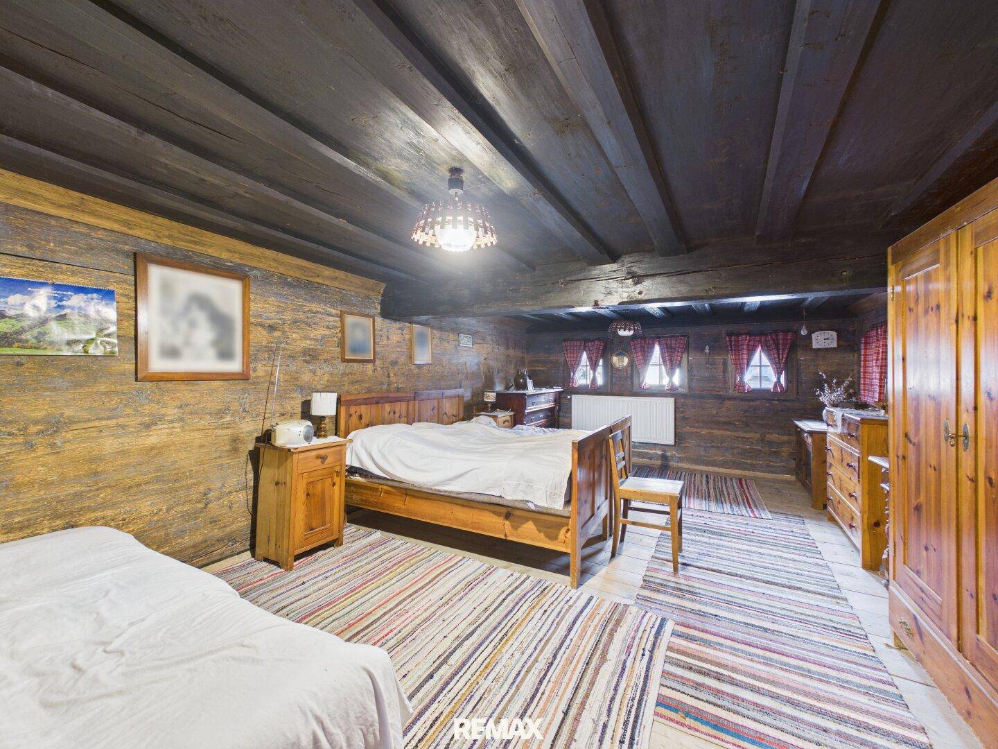 Geräumiges Schlafzimmer mit Holzwänden, Holzbalkendecke und bunten Teppichen.