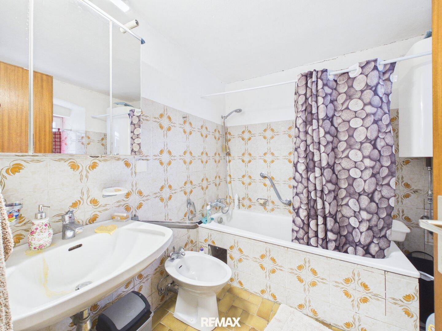 Badezimmer im 80er-Jahre-Stil mit Badewanne, Bidet und gemusterten Fliesen.