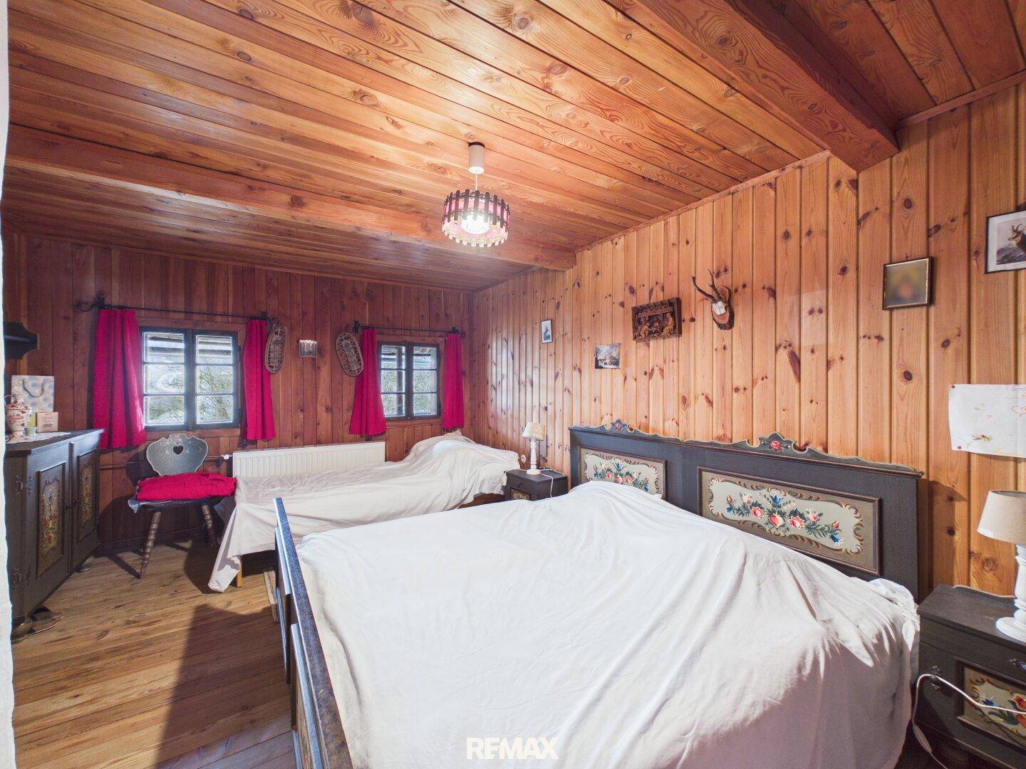 Rustikales Schlafzimmer mit Holzvertäfelung, Holzboden und traditionell bemalten Betten.