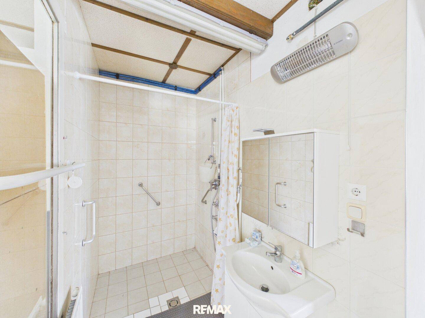 Badezimmer mit Duschkabine, Waschbecken und Wandfliesen, mit Haltegriffen.
