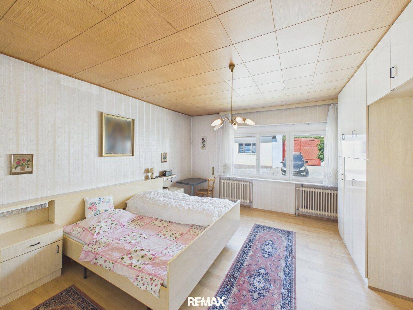 Schlafzimmer mit Holzpaneeldecke, Doppelbett und Einbauschränken, hell durch großes Fenster.