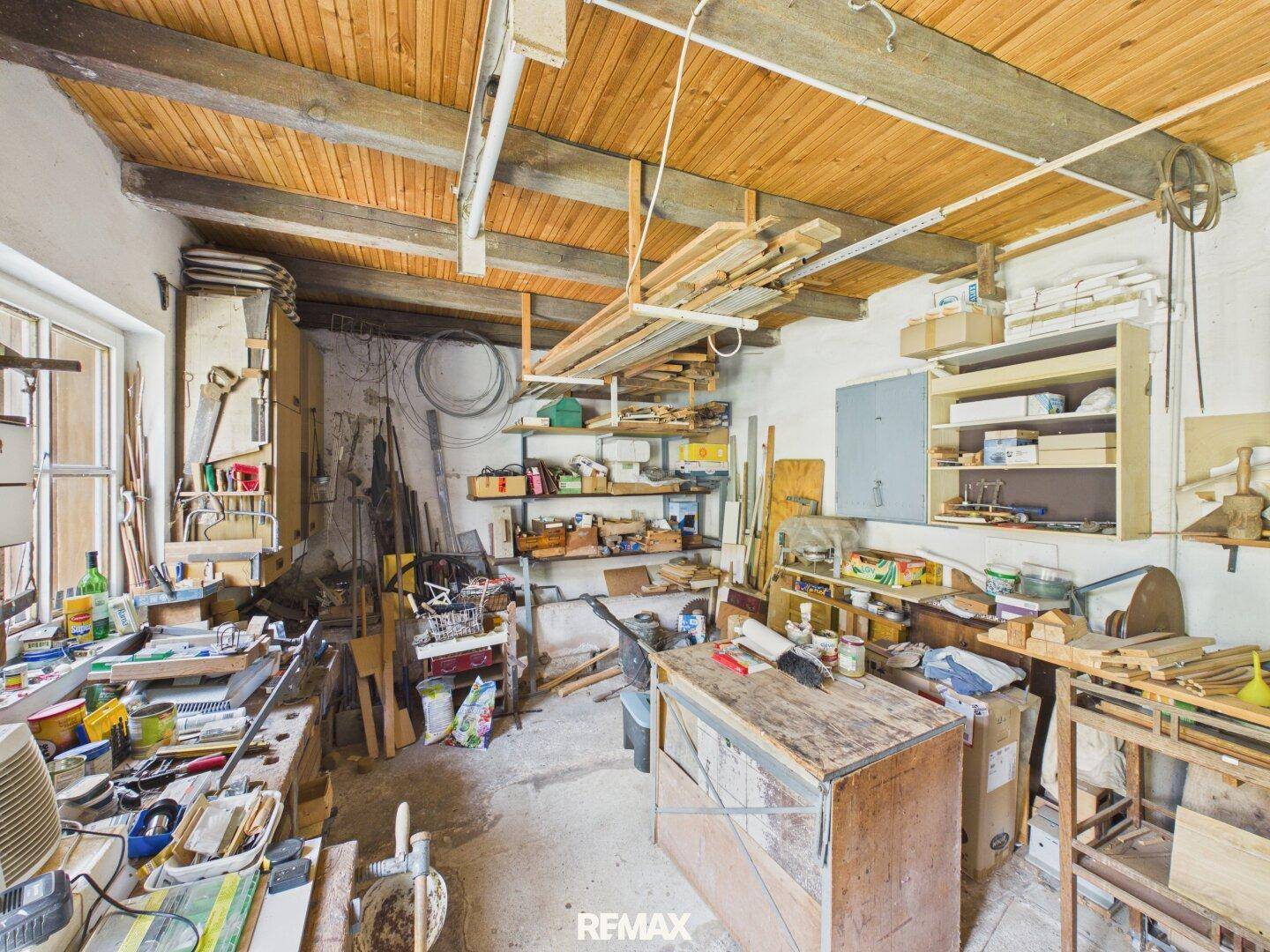 Werkstattraum mit Holzbalkendecke, vielen Werkzeugen und Materialien, gut beleuchtet.