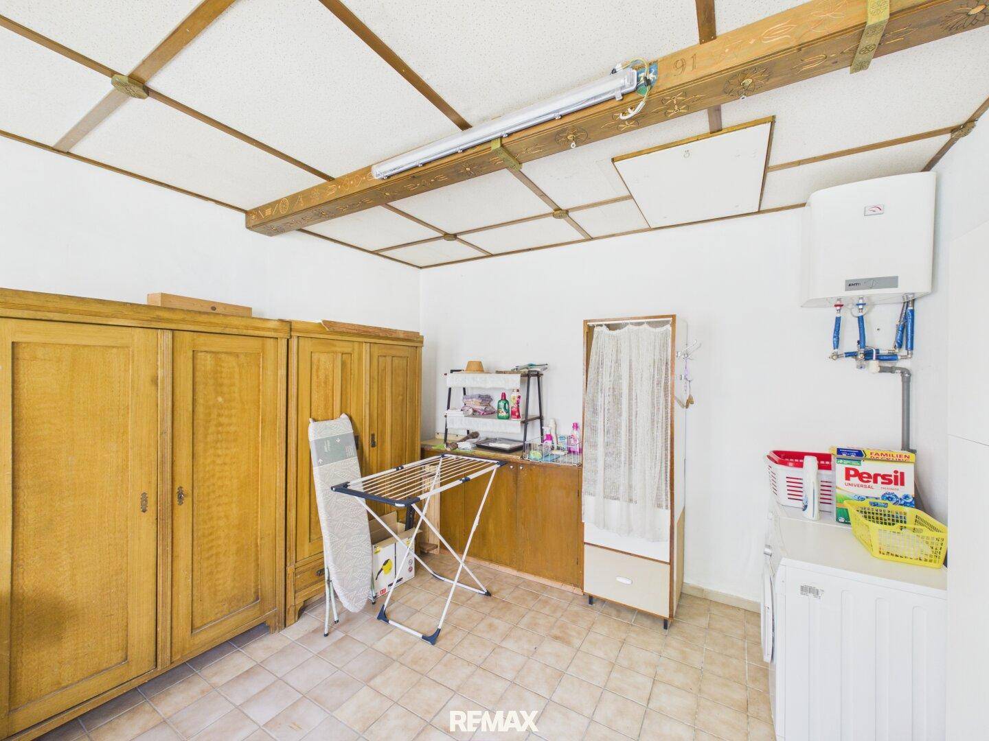 Hauswirtschaftsraum mit Waschmaschine, Trockenständer und Holzschränken, gefliestem Boden.