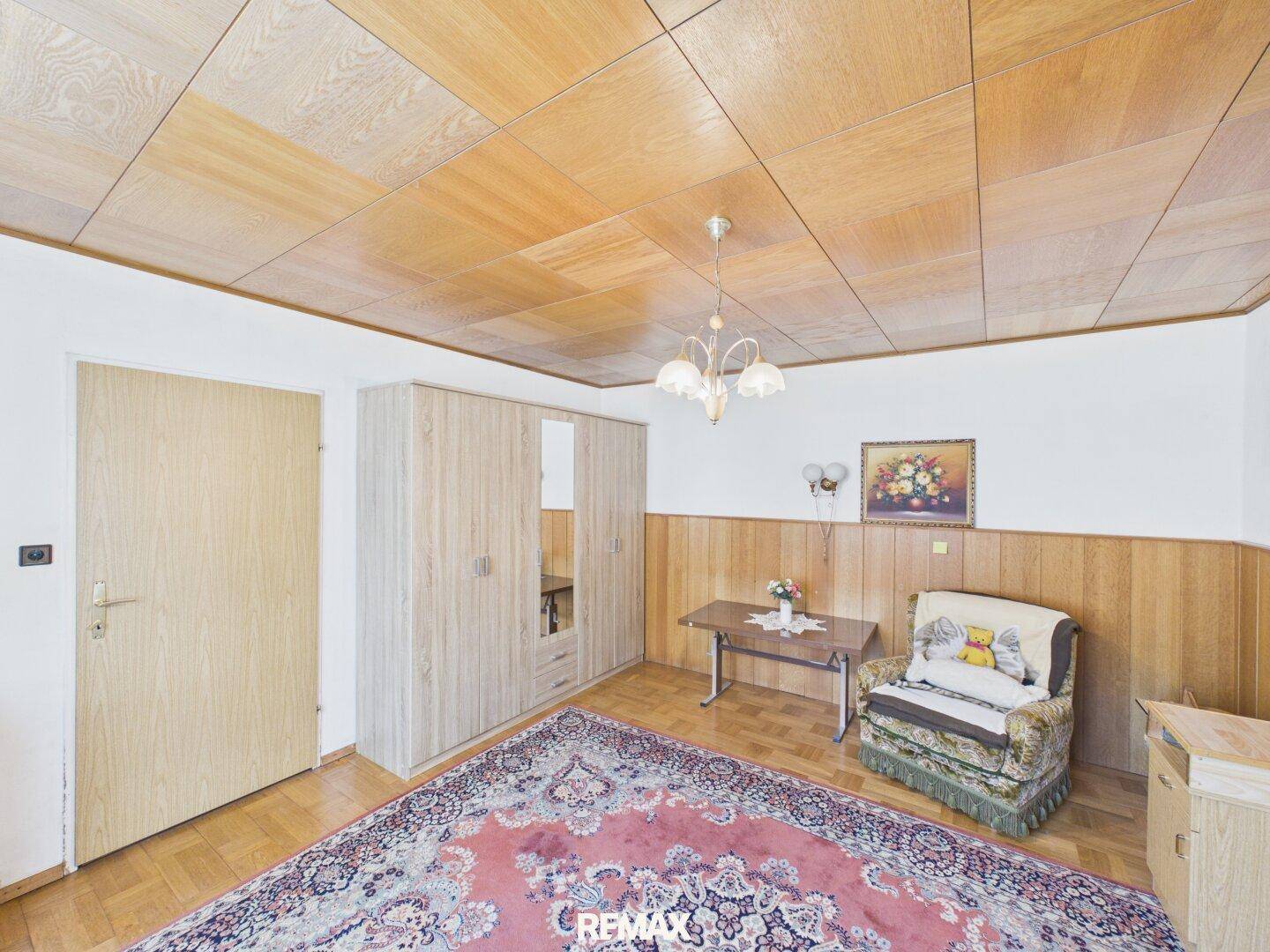 Schlafzimmer mit Holzpaneeldecke, Teppich und einem Kleiderschrank, mit Holzvertäfelung.