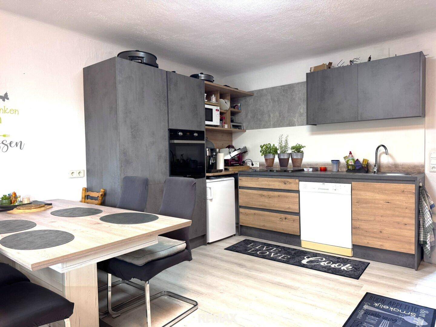 Moderne Küche mit grauen und holzfarbenen Schränken sowie einem integrierten Essbereich.