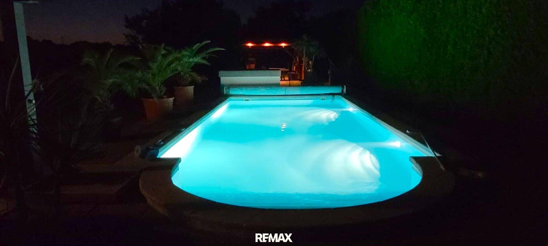 Beleuchteter Swimmingpool bei Nacht mit klarem, türkisfarbenem Wasser und umgebenden Pflanzen.