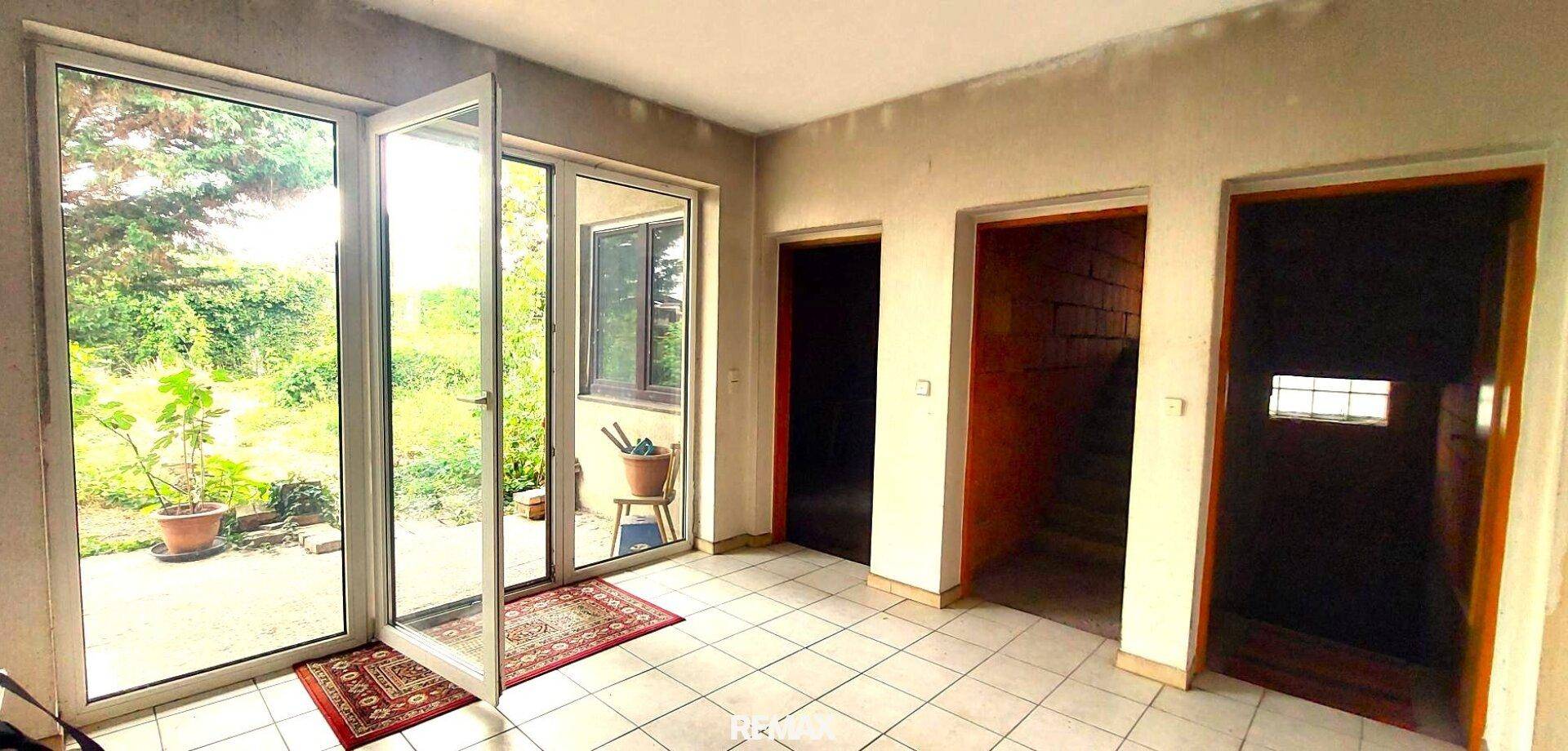 Heller Eingangsbereich mit großen Glastüren zum Garten und Fliesenboden.