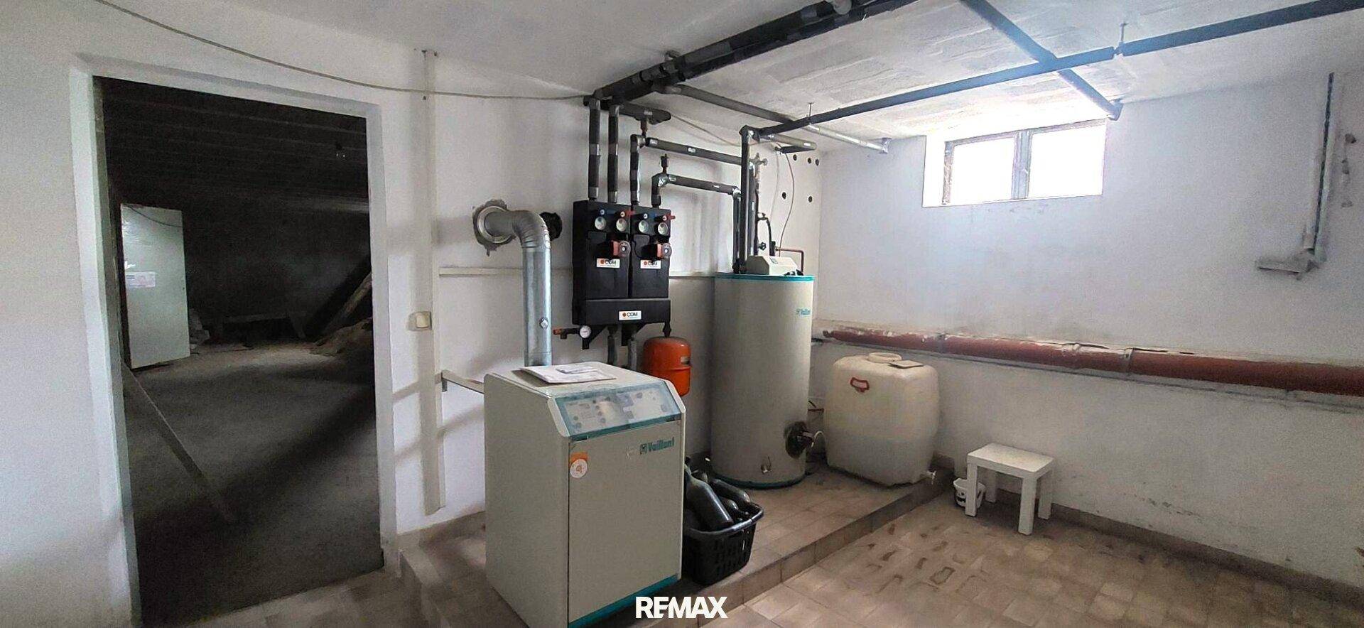 Heizungsraum im Keller mit Heizkessel, Warmwasserspeicher und kleinem Fenster.