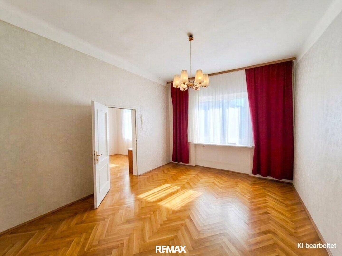Geräumiges Wohnzimmer mit Fischgrätparkett, roten Vorhängen und viel Tageslicht.