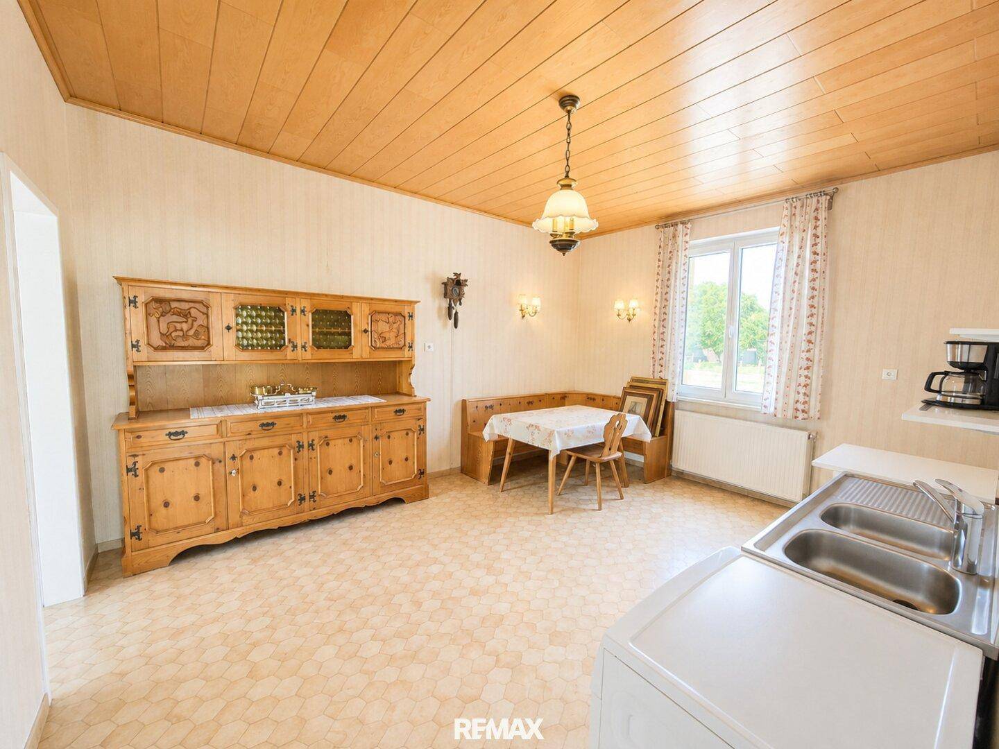 Traditionelle Wohnküche mit Holzdecke, Einbauschrank und gemütlicher Essecke am Fenster.
