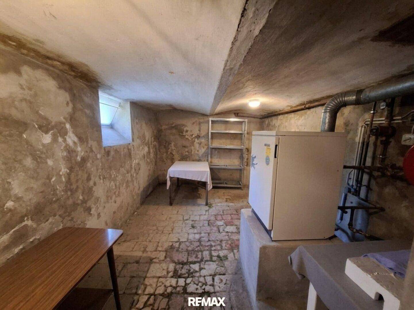 Rustikaler Kellerraum mit Ziegelboden, kleinem Fenster und Heizungsanlage.