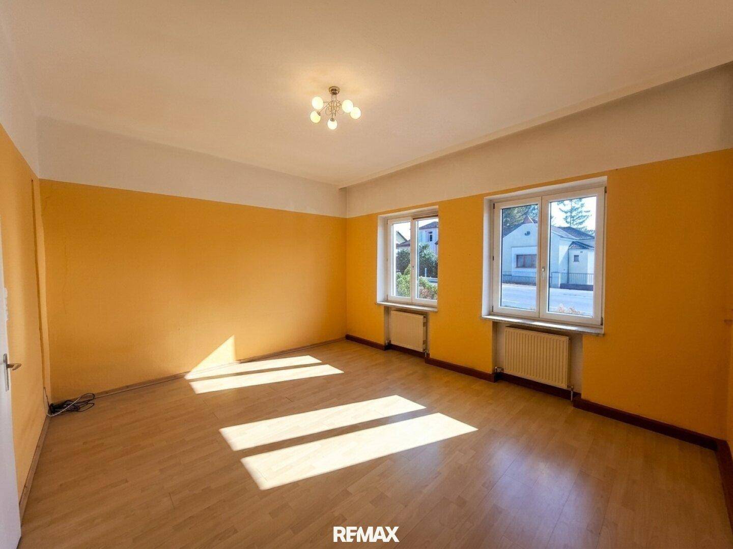 Geräumiges Zimmer mit gelben Wänden, Laminatboden und zwei Fenstern für viel Licht.