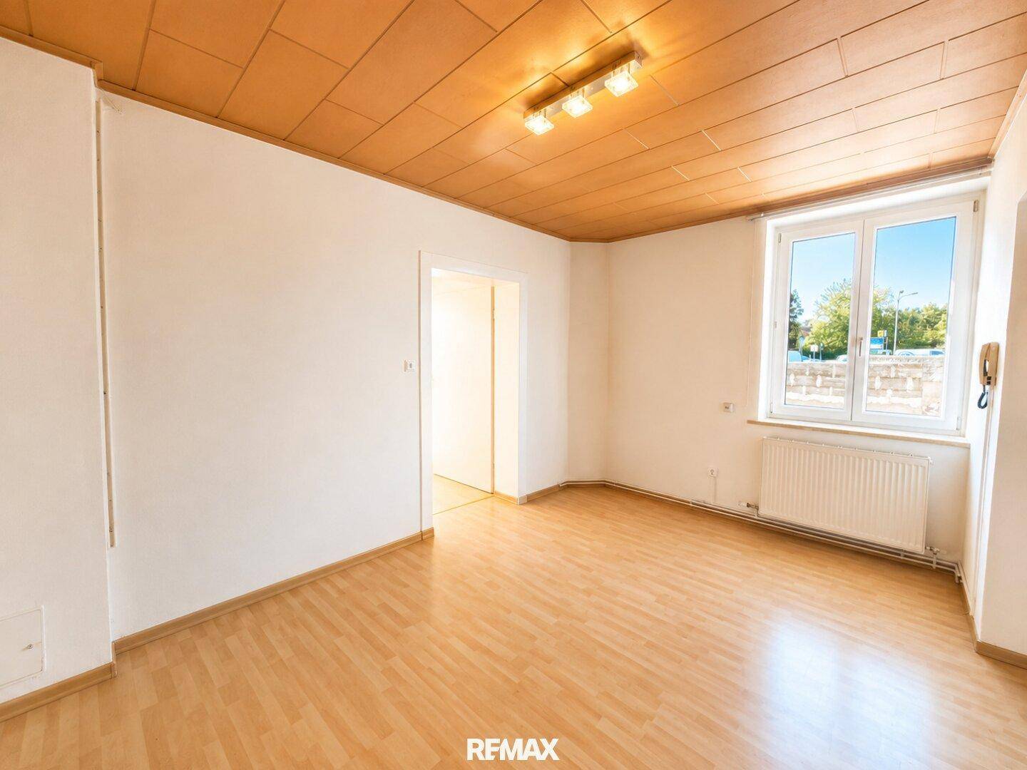 Helles Zimmer mit Laminatboden, Holzdecke und großem Fenster mit Blick ins Grüne.