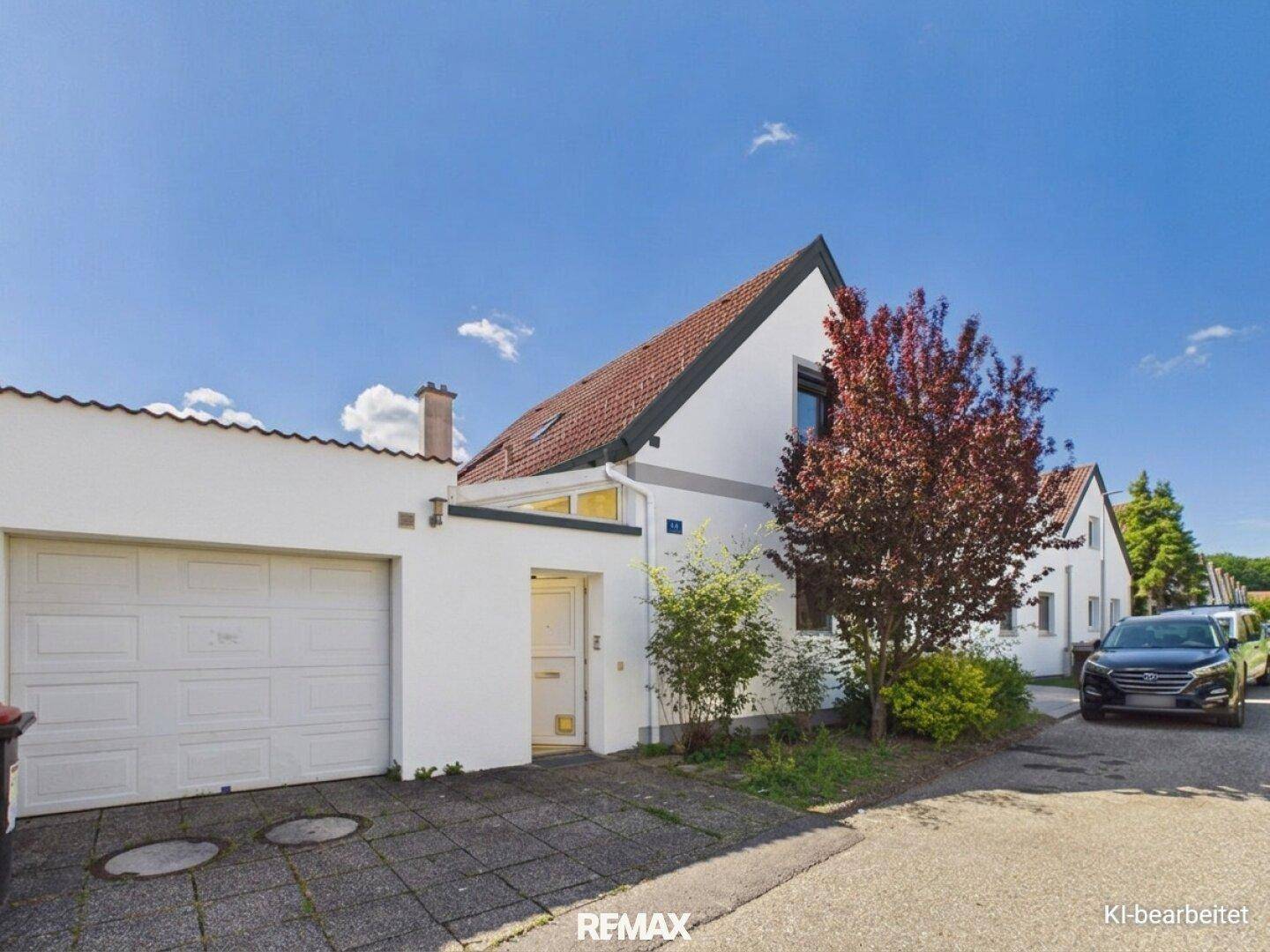 Vorderansicht des Hauses mit integrierter Garage, Einfahrt und einem Baum.