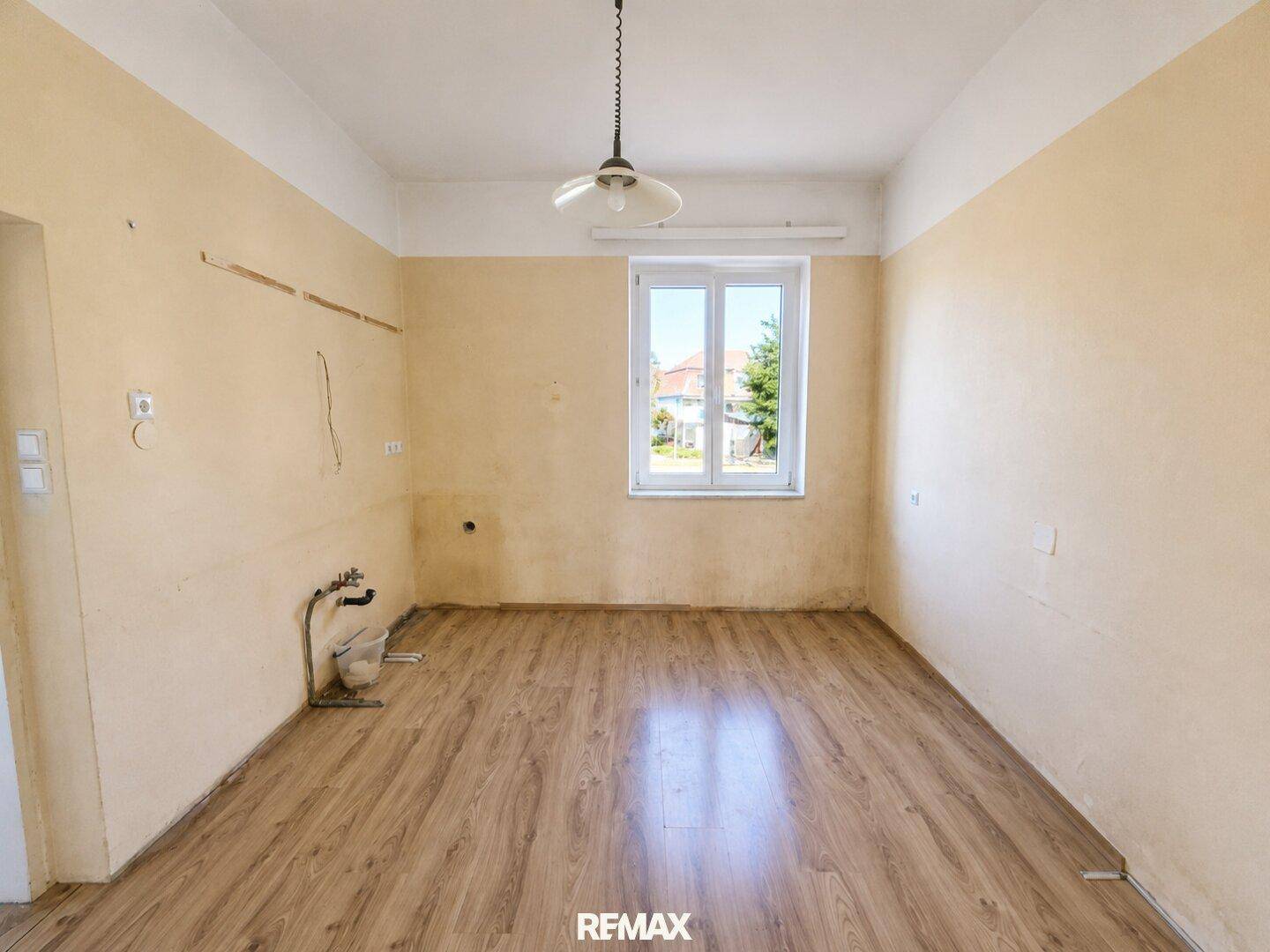 Leerer Küchenraum mit Anschlüssen für Spüle und Fenster, bereit für eine neue Einrichtung.