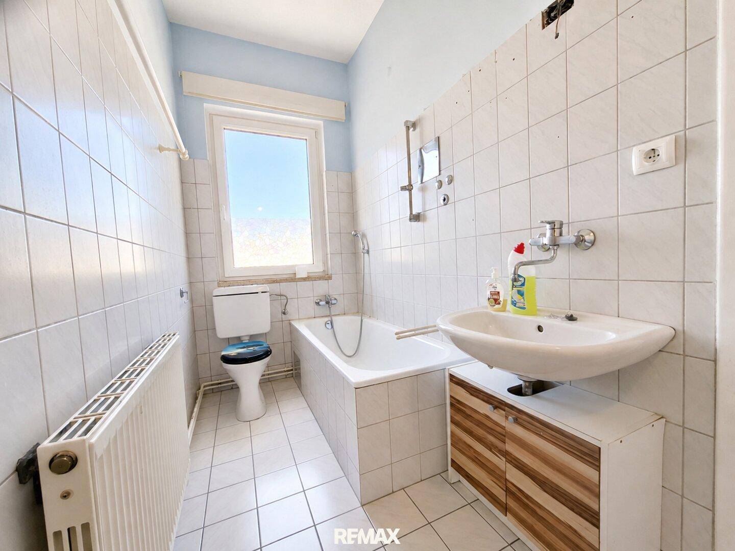 Badezimmer mit Badewanne, WC, Waschbecken, weißen Fliesen und Fenster für Tageslicht.