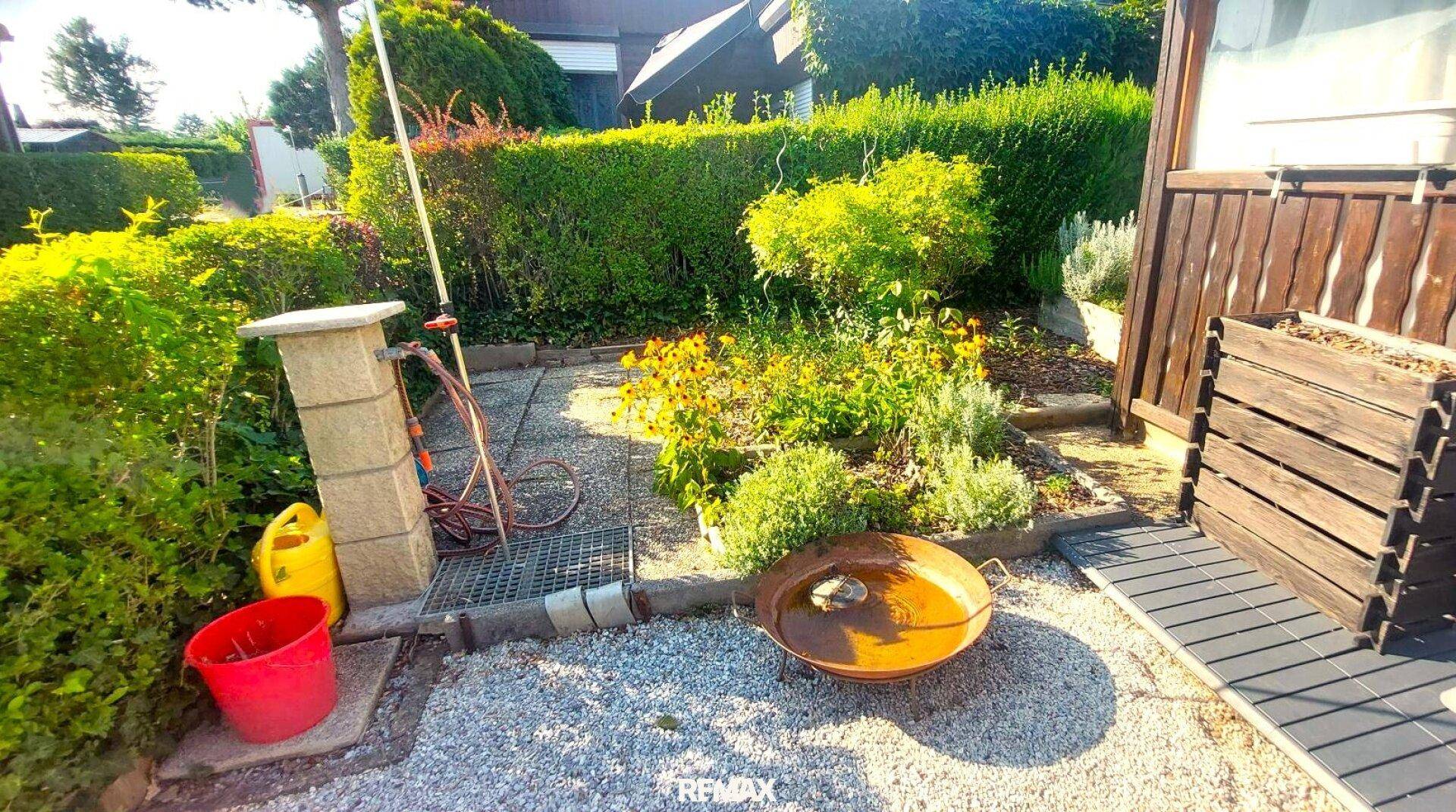 Gepflegter Gartenbereich mit Blumenbeeten, Feuerstelle und Gartenschlauch für gemütliche Abende.