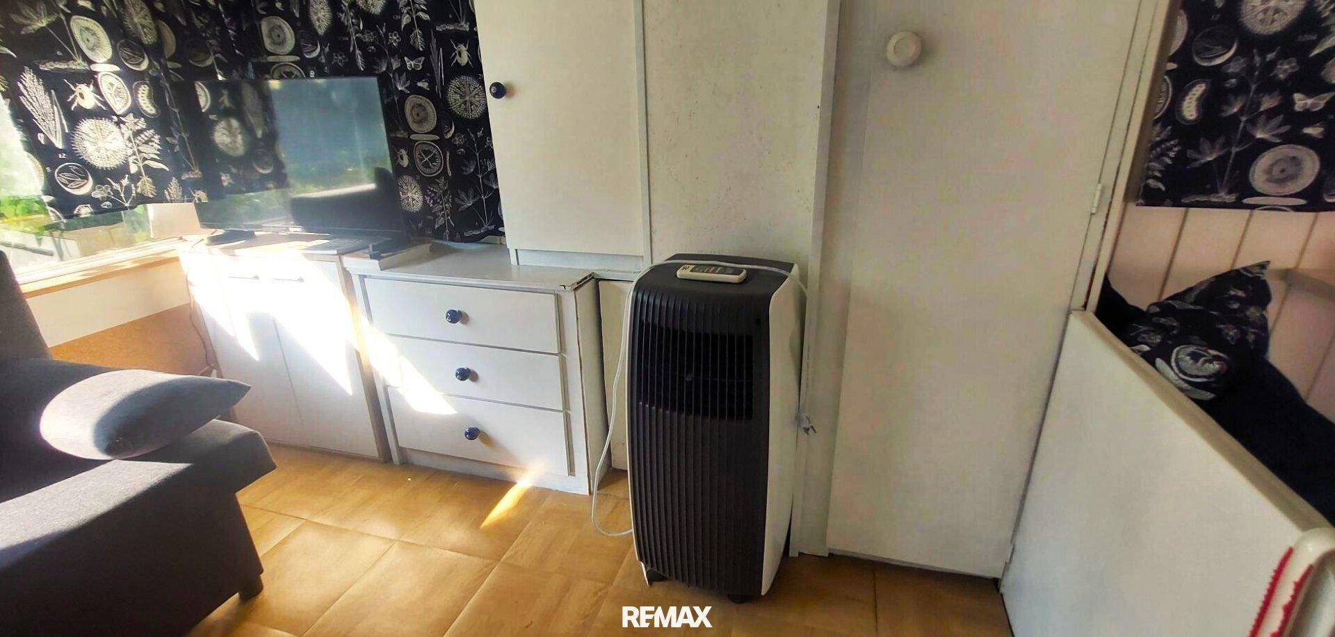 Wohnbereich mit Fernseher, Schränken und einem mobilen Klimagerät für angenehme Temperaturen.