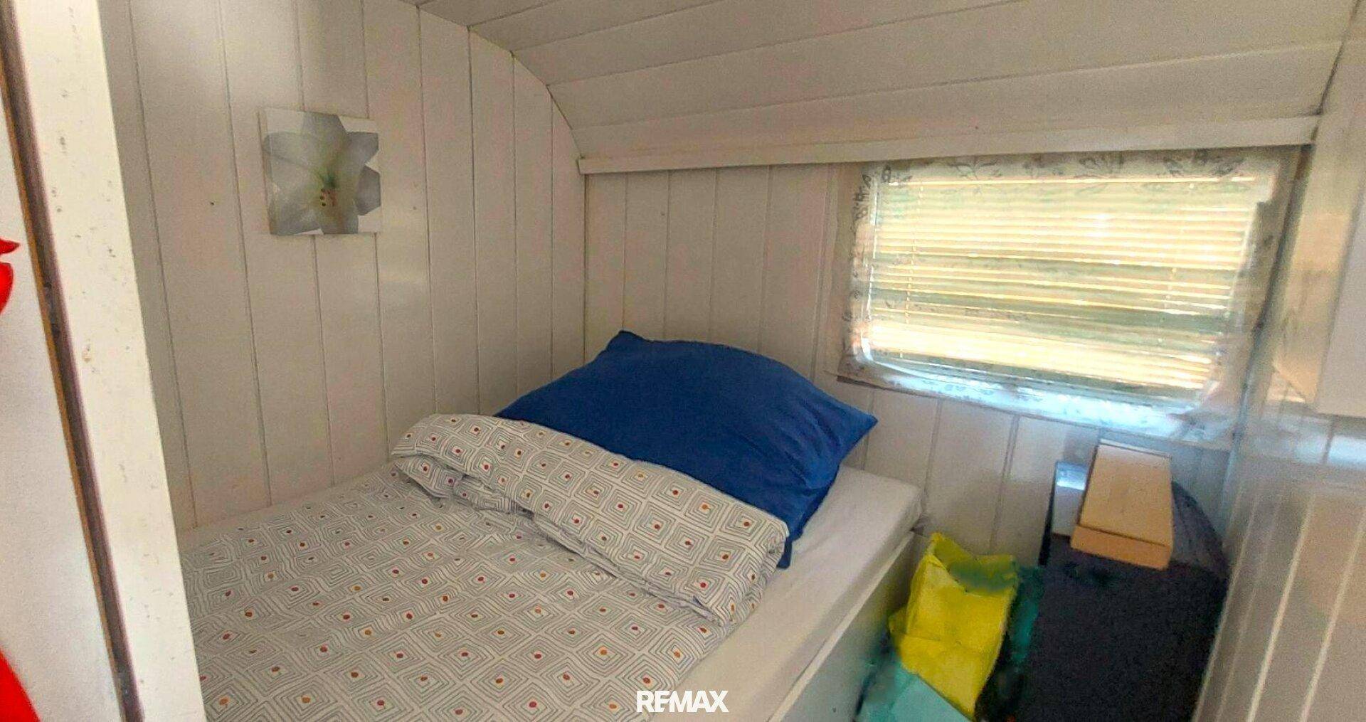 Kleines Schlafzimmer mit Einzelbett und Fenster, ideal als Gästezimmer mit Holzdecke.