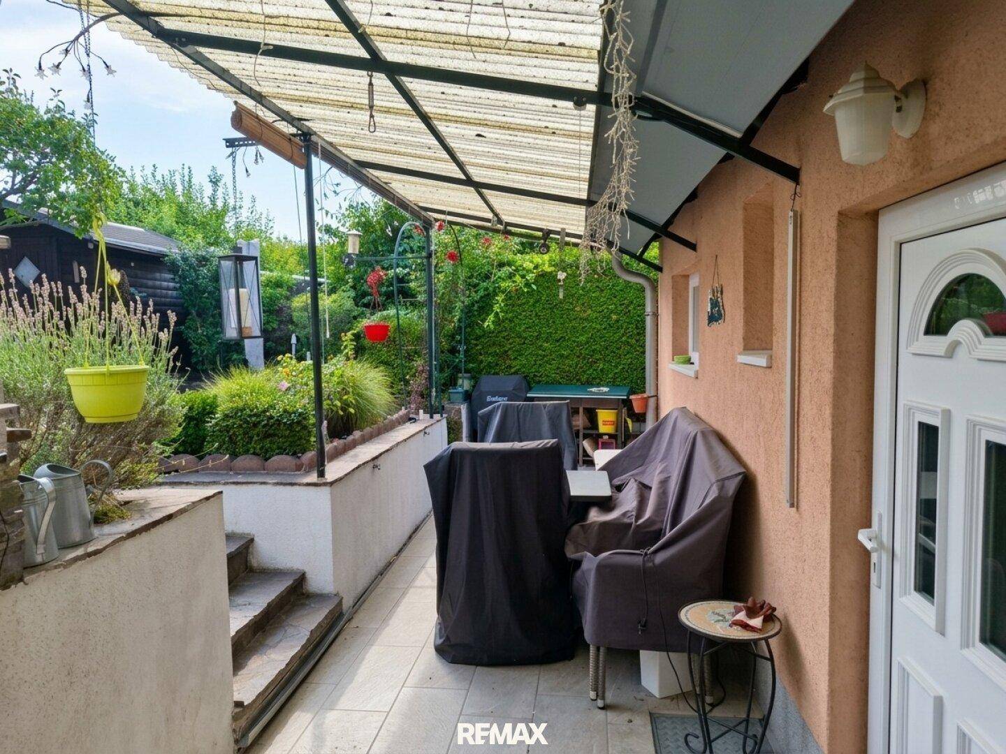 Überdachte Terrasse mit Fliesenboden und Gartenmöbeln, ideal für entspannte Stunden im Freien.