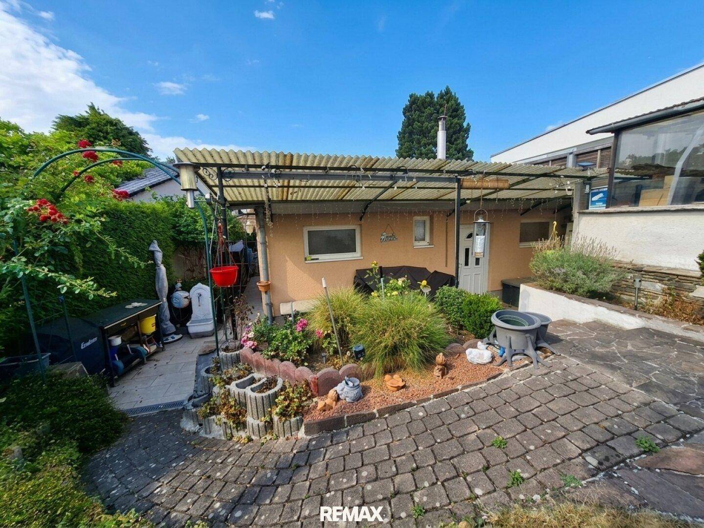 Kleiner, liebevoll gestalteter Gartenbereich hinter dem Haus mit überdachtem Sitzplatz und Blumenbeeten.