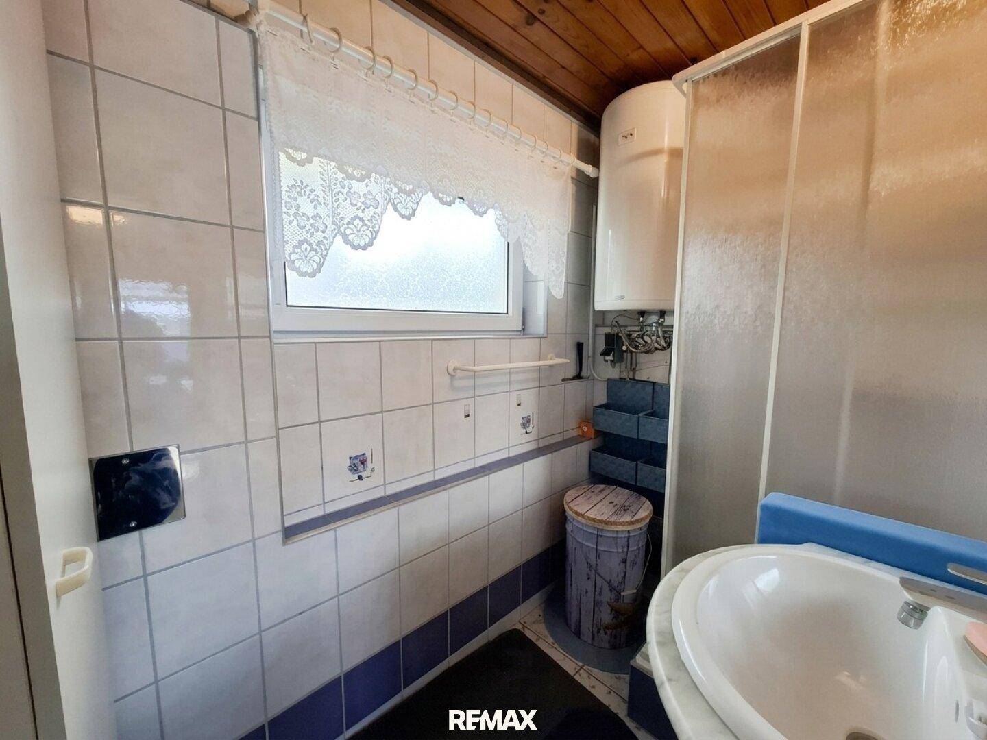 Badezimmer mit Dusche, Waschbecken und Fenster, gefliest in hellen und blauen Tönen.