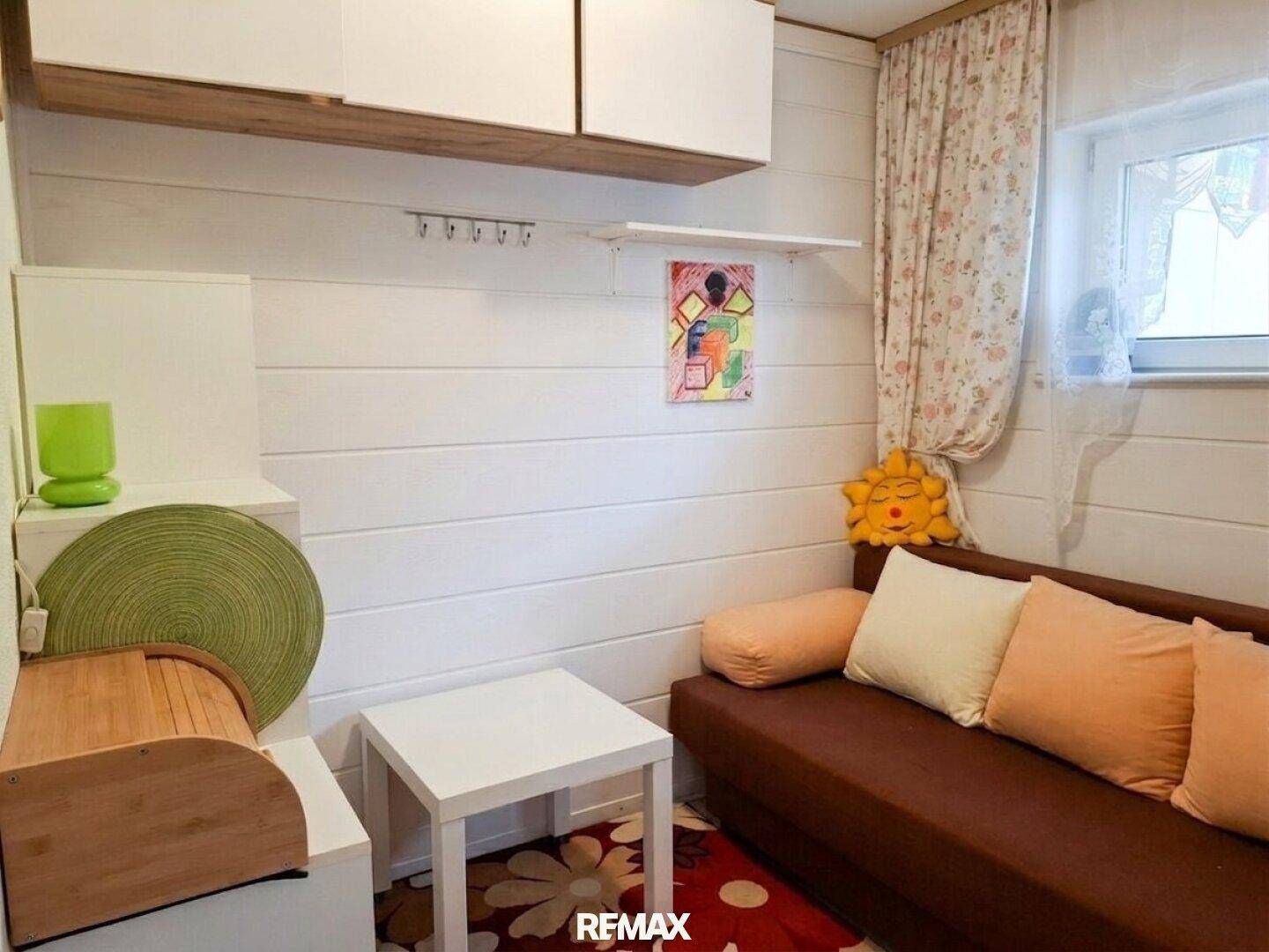 Helles Zimmer mit Sofa, weißen Holzpaneelen und einem Fenster, ideal als Gästezimmer.