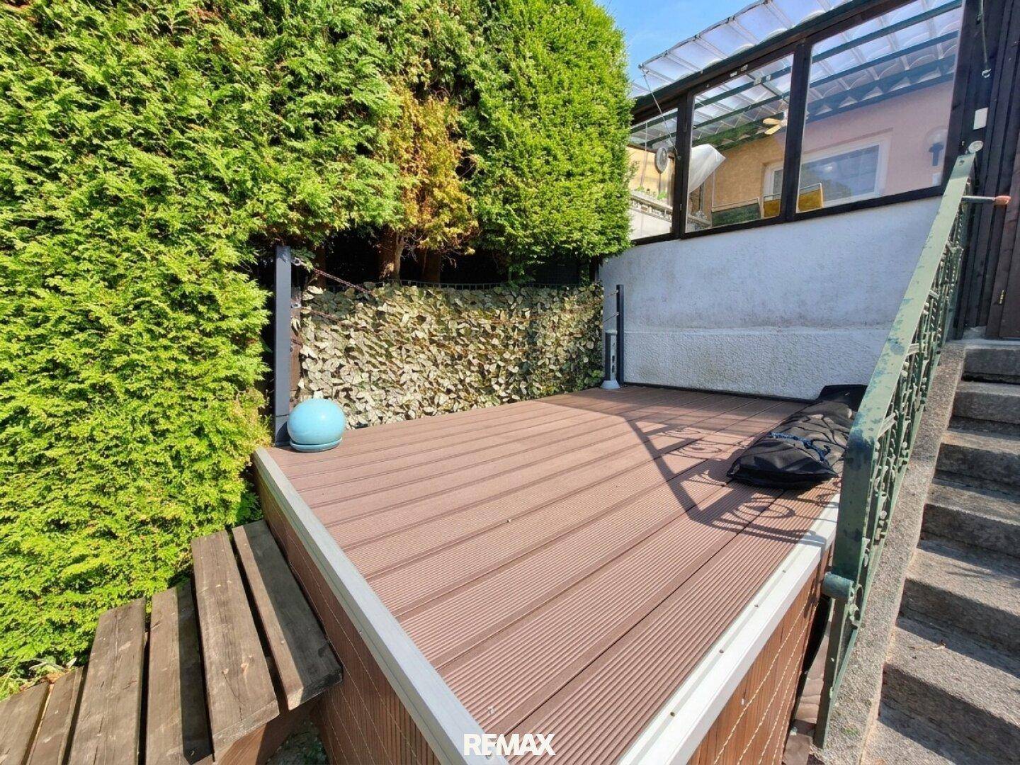 Holzterrasse mit Treppenzugang, umgeben von einer hohen Hecke, bietet Privatsphäre.